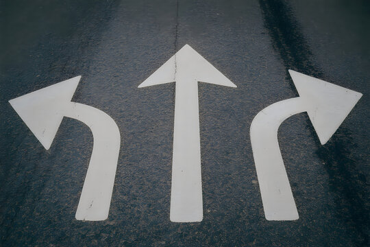 White painted directional arrows on dark textured asphalt road surface