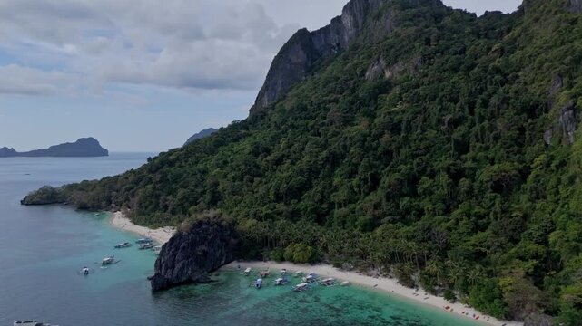 Cinematic drone flight moving backwards and upwards from Papaya Beach. Expanding view of limestone cliffs, turquoise water and the El Nido coastline.