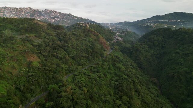 Scenic aerial flyover of a winding mountain road cutting through dense forest and rolling hills along Asin Road, Benguet, Philippines.