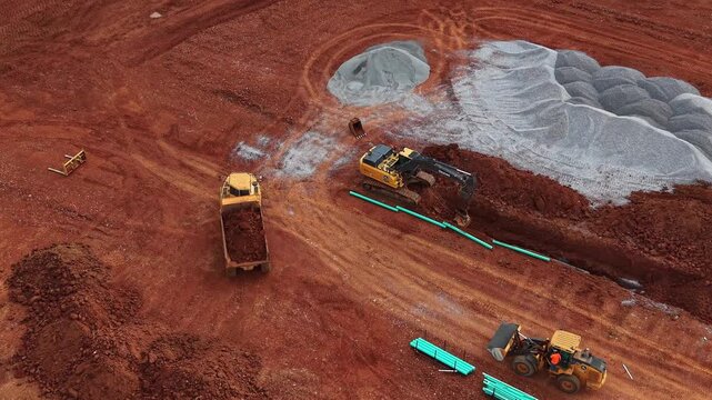 Aerial drone footage of a dump truck going in reverse, while an excavator continues to dig trenches at a newly developed construction site