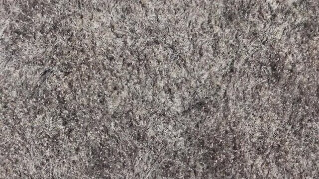 A high-angle aerial view showcases a vast expanse of dried tundra grass and dormant winter vegetation. This natural texture highlights the desolate beauty of a cold, barren landscape during autumn.
