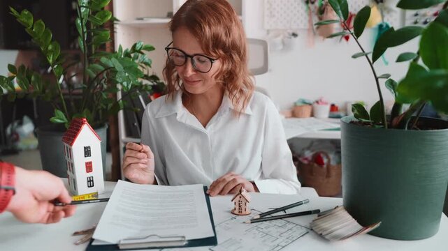 Young realtor consulting customer desk with housing documents, blueprint, miniature house. Signing rental sales agreement, professional property service, secure investment process. Signing contract.