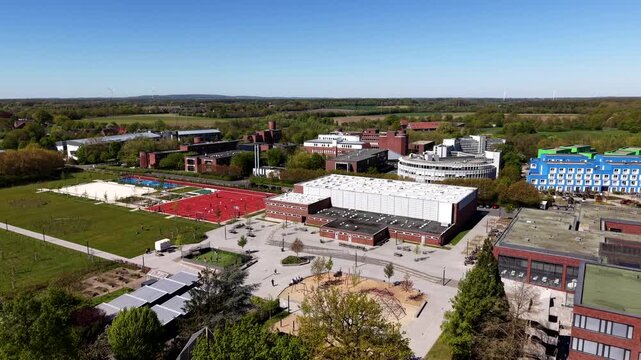 Aerial approaching of university campus in American town with sport fields and colored dormitory houses. Sunny day in spring season. Small town of USA. Wide shot. Red brick facade building of school.
