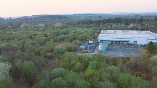 Sideways Aerial View Over Run Down Warehouse with Loading Bays Surrounded by Forest Landscape. Industrial Infrastructre Surrounded by Natural Environment. 4K.