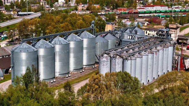 Aerial view of large grain silos beside a railway in an urban industrial area, showing agricultural storage, metal tanks, and logistics infrastructure.