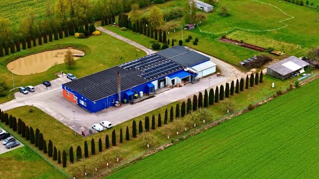 Aerial view of a rural commercial building with rooftop solar panels, surrounded by manicured grounds, farm fields, and tree-lined property roads.