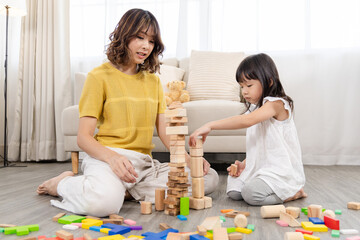 Naklejka premium mother, daughter, family, education, homeschool child playing wooden toy block tower at home, developing intelligence and knowledge through creativity learning activity, early preschool motor skills