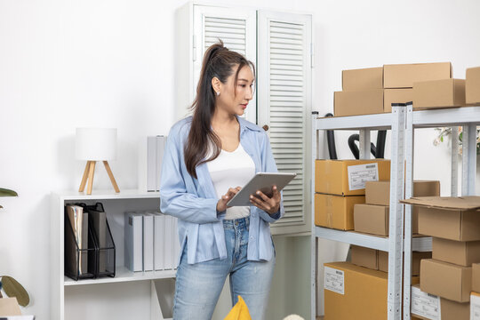 Inventory, stock, storage, warehouse, tracking, retail small business entrepreneur woman uses tablet beside parcel rack, checking products in home-based office or stockroom, keeping organized workflow