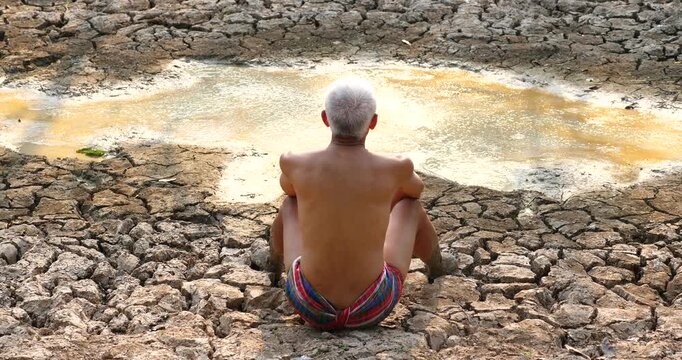 A farmer sits gazing at a dried-up lake; the farmer is sad; climate change concept.