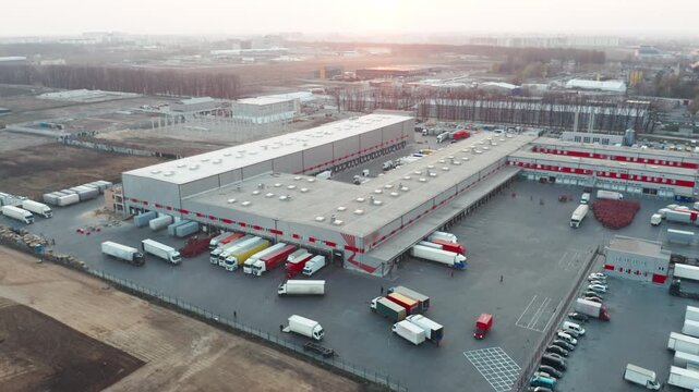 Aerial Drone View: Large Modern Logistics and Distribution Hub with Trucks at Loading Docks at Sunset | Warehouse Complex, Supply Chain and Freight Transportation Concept