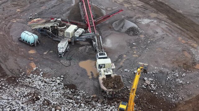 aerial view of vibrating screen stone crusher in active operation at a quarry near Halifax, Nova Scotia. Heavy mobile machinery crushes limestone and minerals for Canadian construction industry 4K.