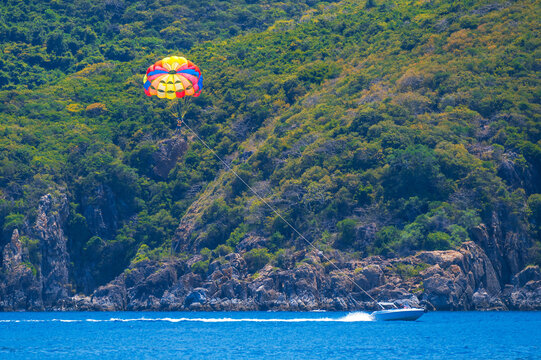 Parasailing at sea in summer on vacation at resort. Extreme water sports. A man parachutes behind a boat