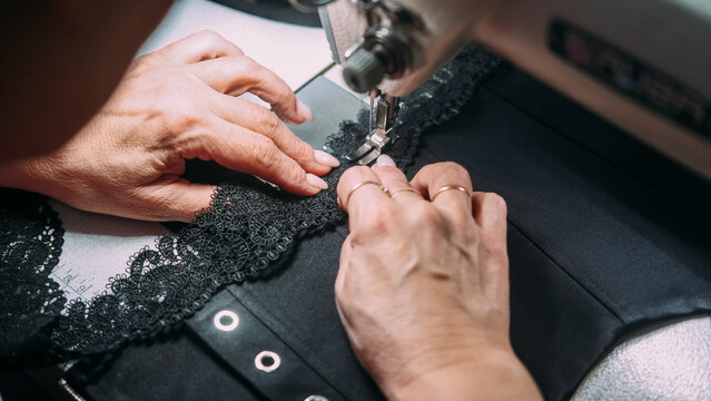 Tailoring process. Sewing lace. Seamstress hand making black fabric corset on stitching machine. Professional clothes atelier production.