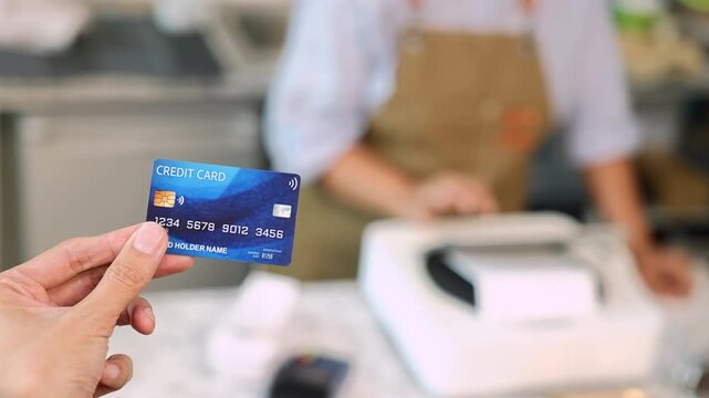 Senior entrepreneur cafe owner barista hold POS machine to customer, Asian female in apron welcome warmly in counter, croissants and glassware background, retired elderly woman start small business