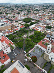 Obraz premium Vertical drone view of Tlaquepaque, Mexico, displaying its historic main square, colonial buildings, and urban life under an overcast sky.
