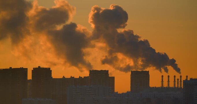 Multiple industrial chimneys release giant steam cloud above urban apartment blocks in glowing evening light Dramatic city skyline with haze energy infrastructure district heating and city atmosphere