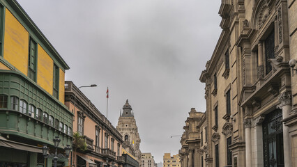 Fototapeta premium Old Spanish colonial architecture. The street of the historical quarter of Lima. Stone buildings with columns, balconies, carvings on the facades. The bell tower of the cathedral against the sky. Peru