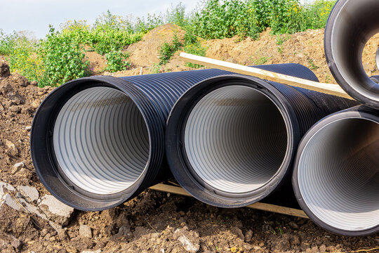 Large diameter corrugated plastic sewer pipes for main pipeline stored on wooden supports at construction site ground