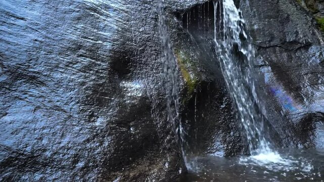 A gentle waterfall flows down a dark wet rock wall in a natural cave