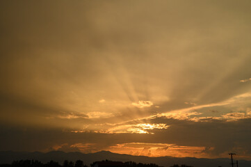 Obraz premium Golden sunset casts a warm glow over distant mountains and dramatic clouds in a tranquil evening sky