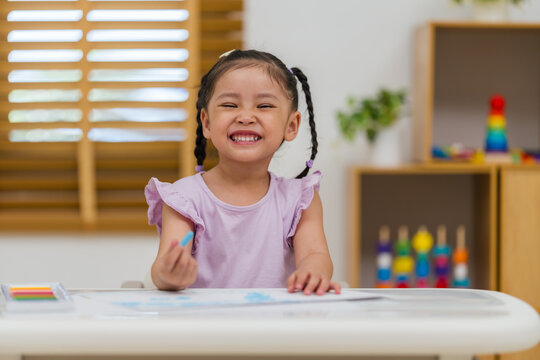 happy preschool child girl drawing and painting with colorful oil pastels on paper
