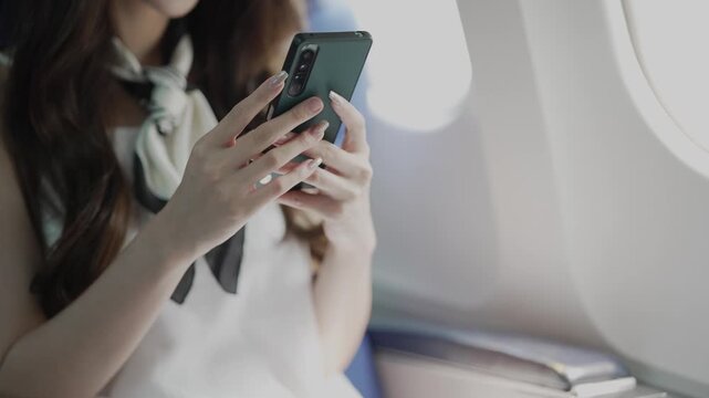 A businesswoman is making a phone call during a flight near the window, contacting a friend while traveling.