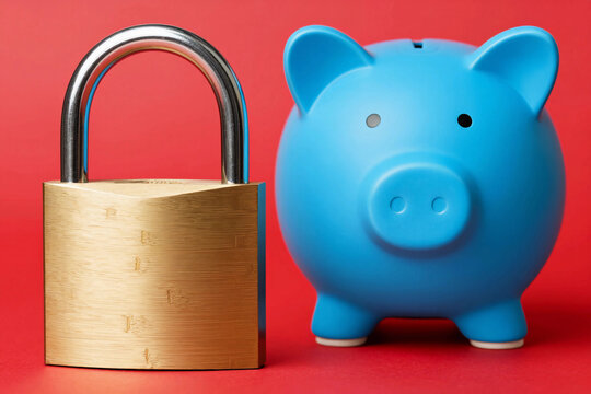 Golden padlock stands beside blue piggy bank. Bright red background highlights security and saving.