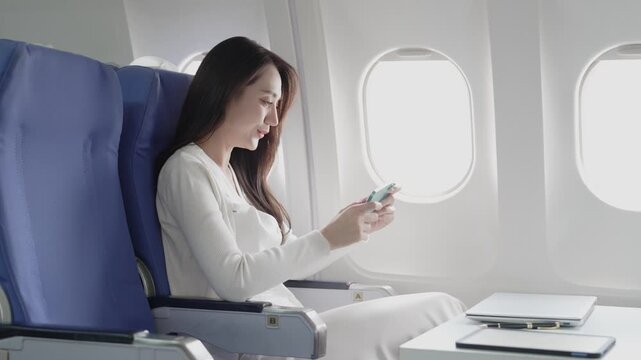 A businesswoman is making a phone call during a flight near the window, contacting a friend while traveling.
