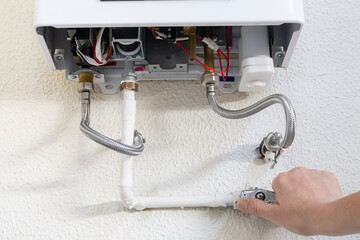 Naklejka premium Professional technician's hand working on plumbing connections and pipes of a gas boiler, servicing a household water heating system requiring careful installation and maintenance