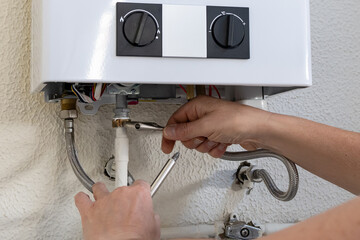 Fototapeta na wymiar Professional plumber hands performing installation or maintenance work on a domestic gas water heater, connecting pipes with tools, ensuring proper functioning and safety