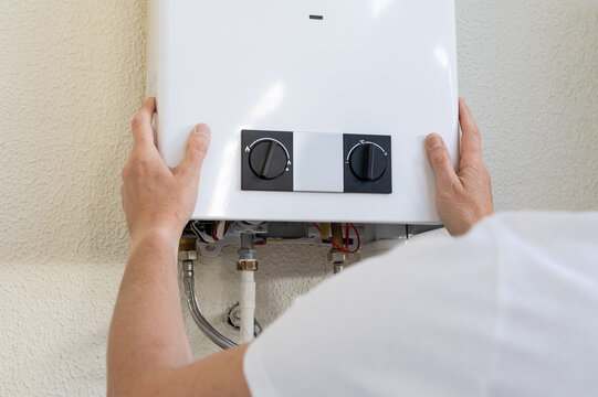 Professional plumber mounting a modern tankless gas water heater on an interior wall, hands connecting pipes and controls during residential installation and efficiency upgrade