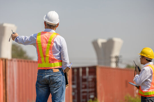Civil engineers in safety gear pointing at construction site with cargo containers, Professional site manager and engineer team monitoring infrastructure development and container terminal operations