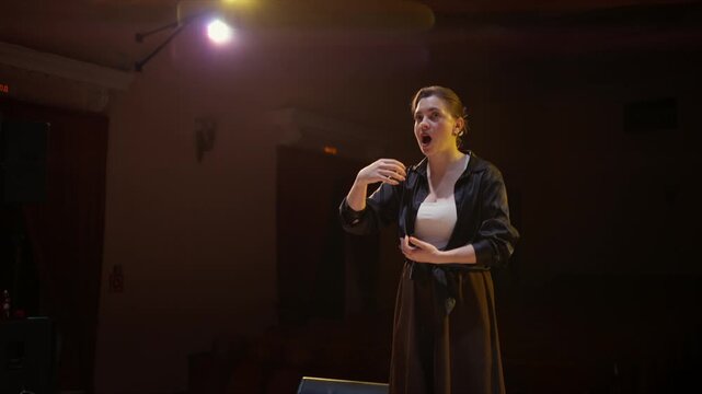Interpreter using expressive sign language on a dimly lit theater stage during a quiet performance rehearsal with attentive observers in the darkened audience