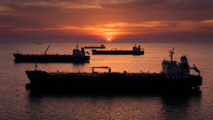Obraz premium Silhouettes of tankers at sunset on tranquil waters 