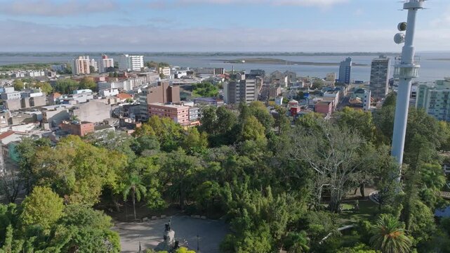 Sideways drone parallax over central park trees revealing Rio Grande city skyline and wide lagoon horizon with sandbar