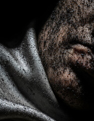Fototapeta premium Dust fabric face portrait close up texture grit darkness low key mystery close up portrait of face covered with black dust silver fabric, intense tactile contrast with low key lighting