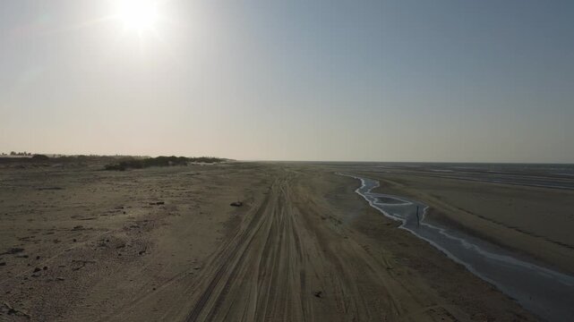 A professional drone moves forward over the wide, sandy beach at Pre&aacute;. The sun shines brightly over the vast coastline, highlighting tire tracks in the sand and small pools of tide water.