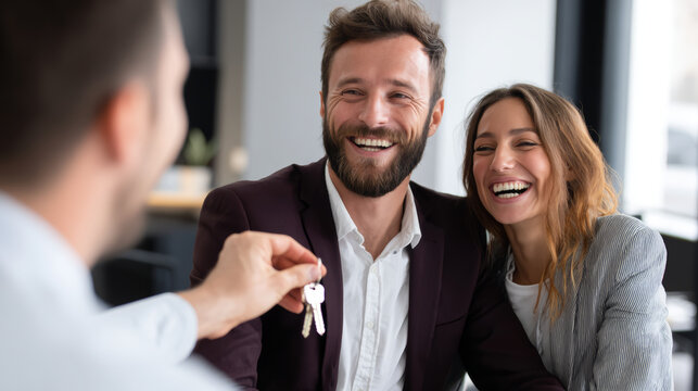 Happy couple receiving house key from real estate agent, smiling man and woman sitting together in office during successful home purchase meeting