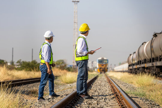 Professional rail inspectors and site managers monitoring train movement and railway infrastructure, Asian engineering team in hardhats and high visibility gear working at industrial railway station