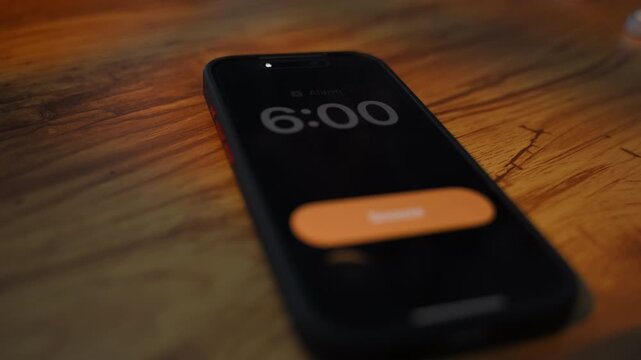 Smartphone alarm clock showing 6:00 on screen. morning wake up concept with mobile phone on the table, hand switching off the alarm