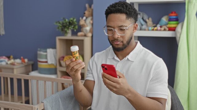 Man holds pill bottle and smartphone while reading the label beside a cradle in a building; concern parental responsibility.