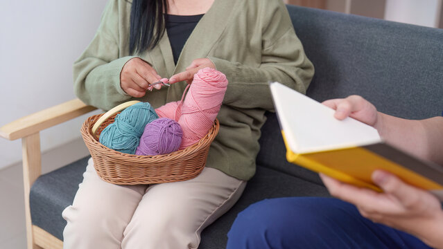 Asian woman senior knitting with caregiver in home for mental wellness