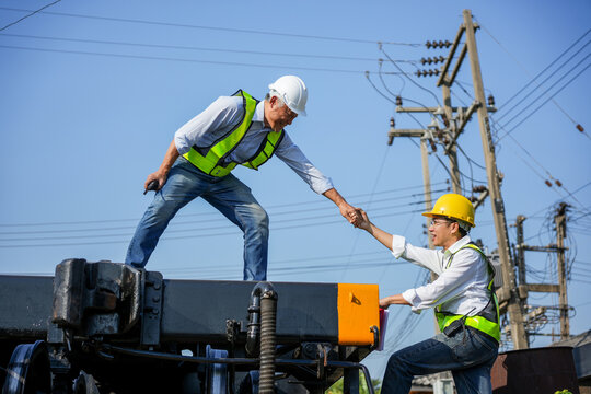 Asian railway engineer helping his colleague to climb up on a freight train car at a railyard, Teamwork and partnership concept with engineers giving a helping hand on a locomotive at industrial site