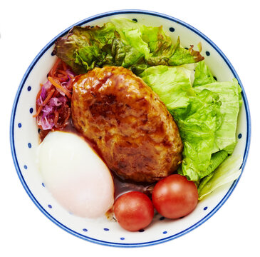 Japanese loco moco bowl with hamburger steak, poached egg, and fresh vegetables in a dotted bowl isolated on white background