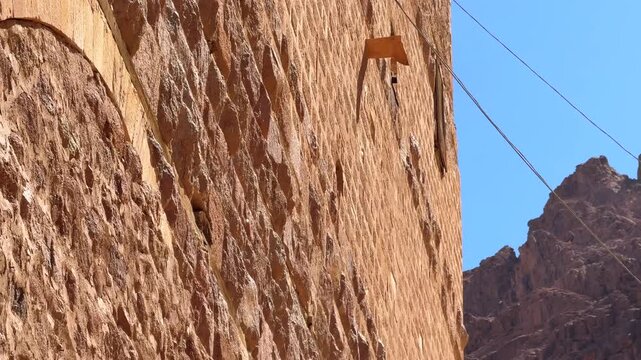 South Sinai, Egypt - November 06, 2025: Saint Catherine Monastery ancient monastery stone wall and Yellow Flag with Christian symbol waving against mountains