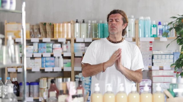 Man is standing in a European pharmacy, he feels a headache and migraine. Customer is standing near a counter with medicines for headaches and pressure drops. High quality 4k footage