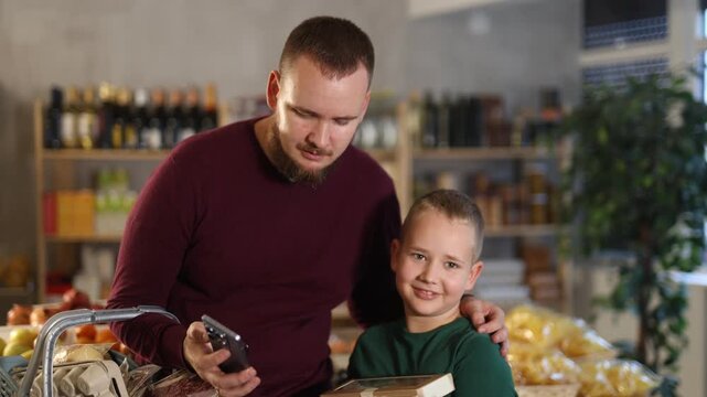 Man and his son are shopping in a supermarket using a phone with an app. Shopper with child with grocery list on phone in grocery store