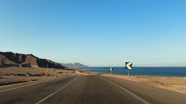 Pov car motion on desert coastal road along the sea with mountains and warning signs