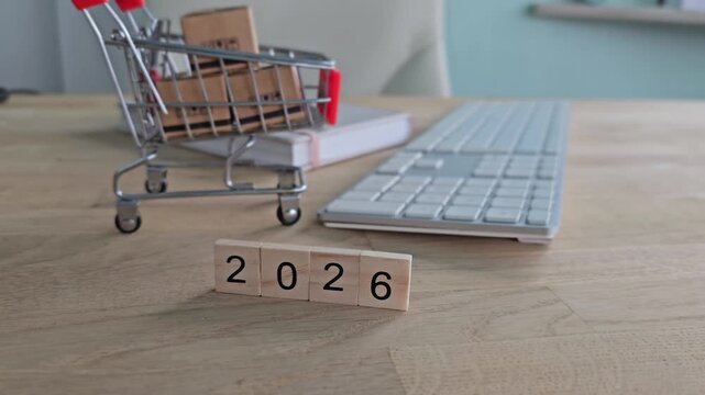 Shopping cart with blocks showing the year 2026 next to a computer keyboard on a wooden table