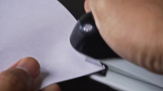 Hands using an office stapler to bind blank documents on a desk representing administrative work